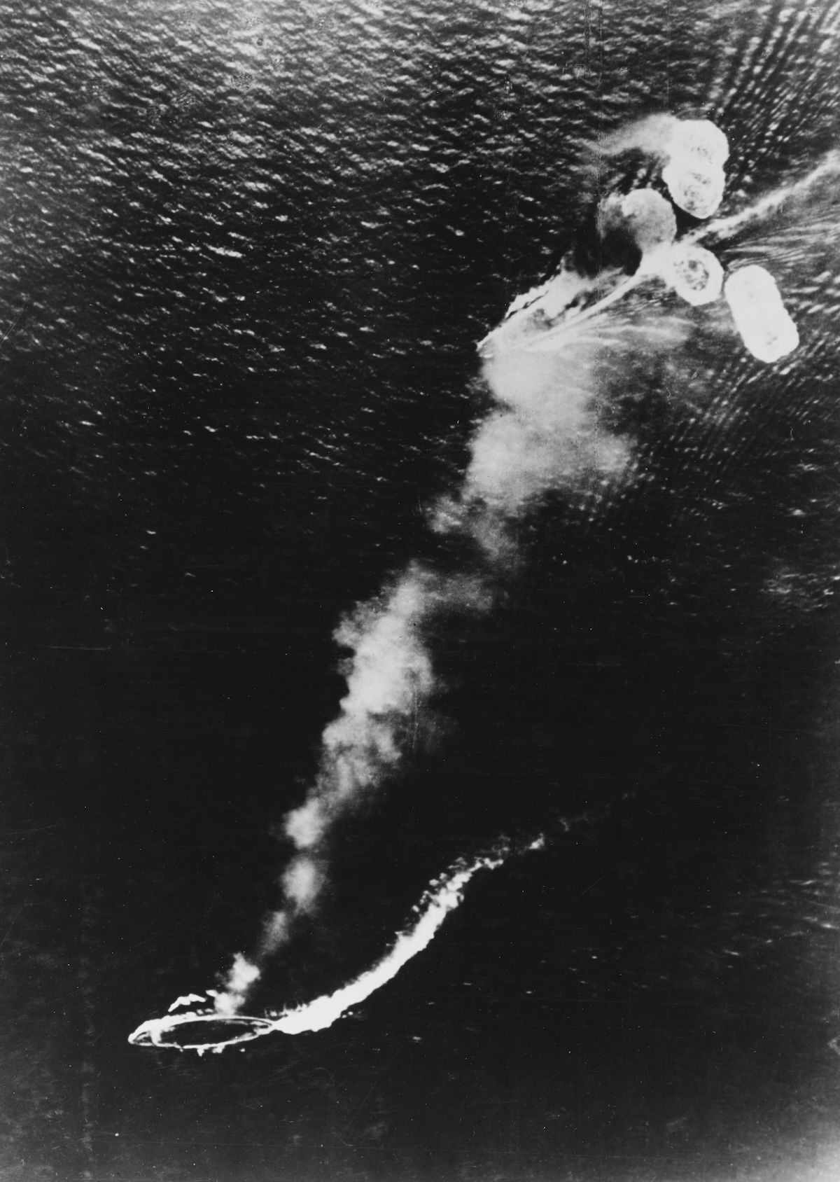 A photograph from a Japanese plane showing damage to HMS Repulse (bottom left) and HMS Prince of Wales (top right), 10 December 1941. US Naval History and Heritage Command. Public Domain.