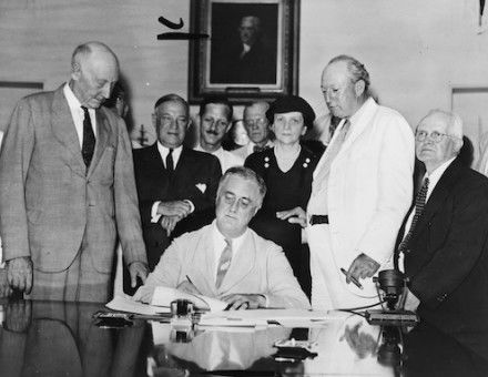 President Roosevelt signs the Social Security Act in the White House, 1935. Harrison is in the white suit. Children's Bureau Centennial (CC BY 2.0)..