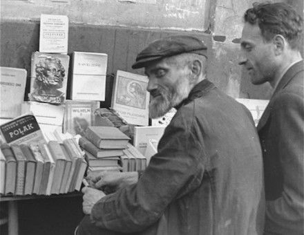 Book vendors sit in front of a table piled with books on a street in the Warsaw ghetto., c. June-August 1941. United States Holocaust Memorial Museum, courtesy of Rafael Scharf.