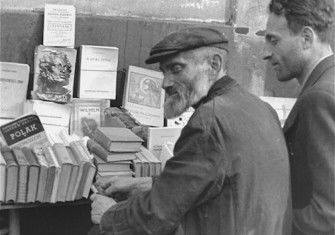 Book vendors sit in front of a table piled with books on a street in the Warsaw ghetto., c. June-August 1941. United States Holocaust Memorial Museum, courtesy of Rafael Scharf.