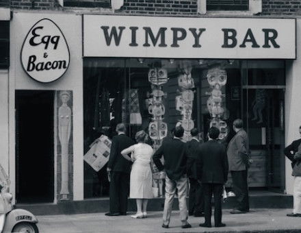 Passers-by looking at a modern sculpture in the window of a Wimpy Bar in London, c.1961. Photograph by John ‘Hoppy’ Hopkins. © Estate of John Hopkins.